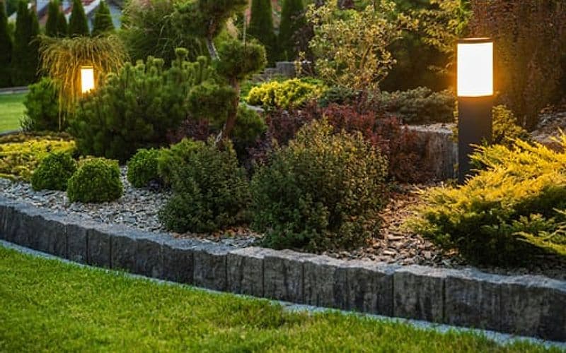 Newly installed landscape beds with layered plantings lit by low-voltage path lighting at dusk